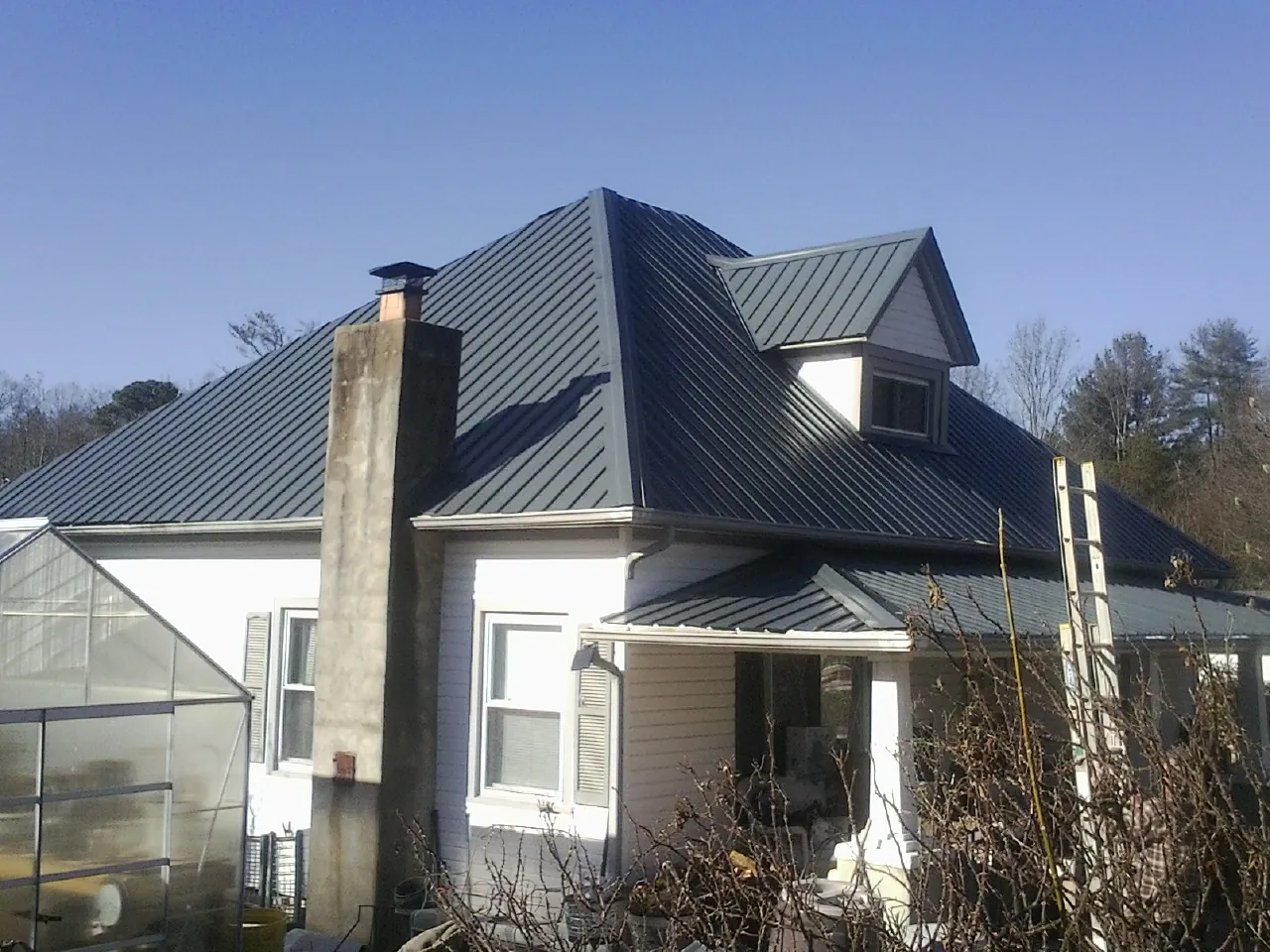 Dark blue standing seam metal roof on a white farmhouse with dormer — Slate & Tile Roof Repair by Roofing Brothers in Leggett