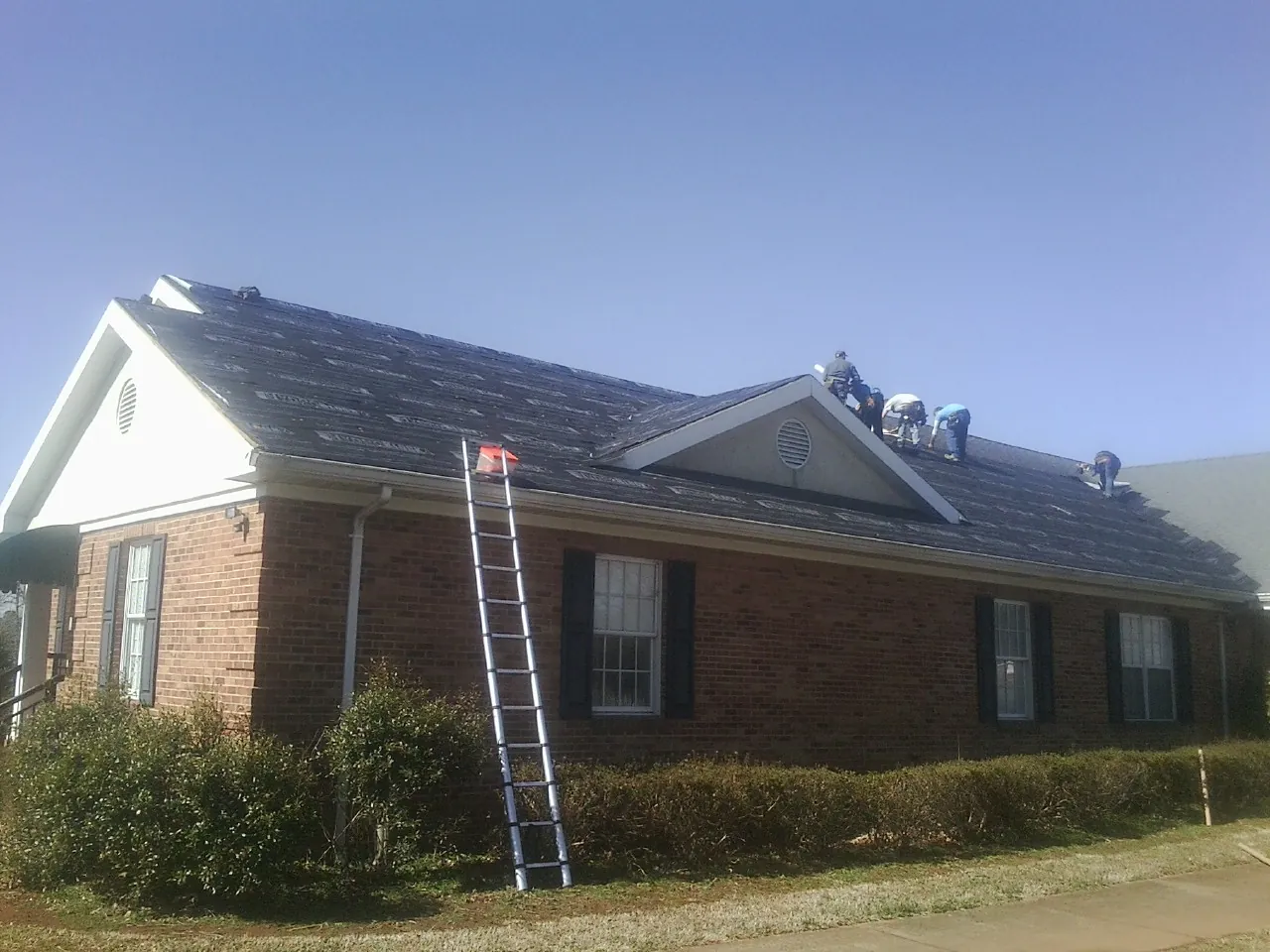Crew tearing shingles off a brick ranch roof with a ladder set in Leggett