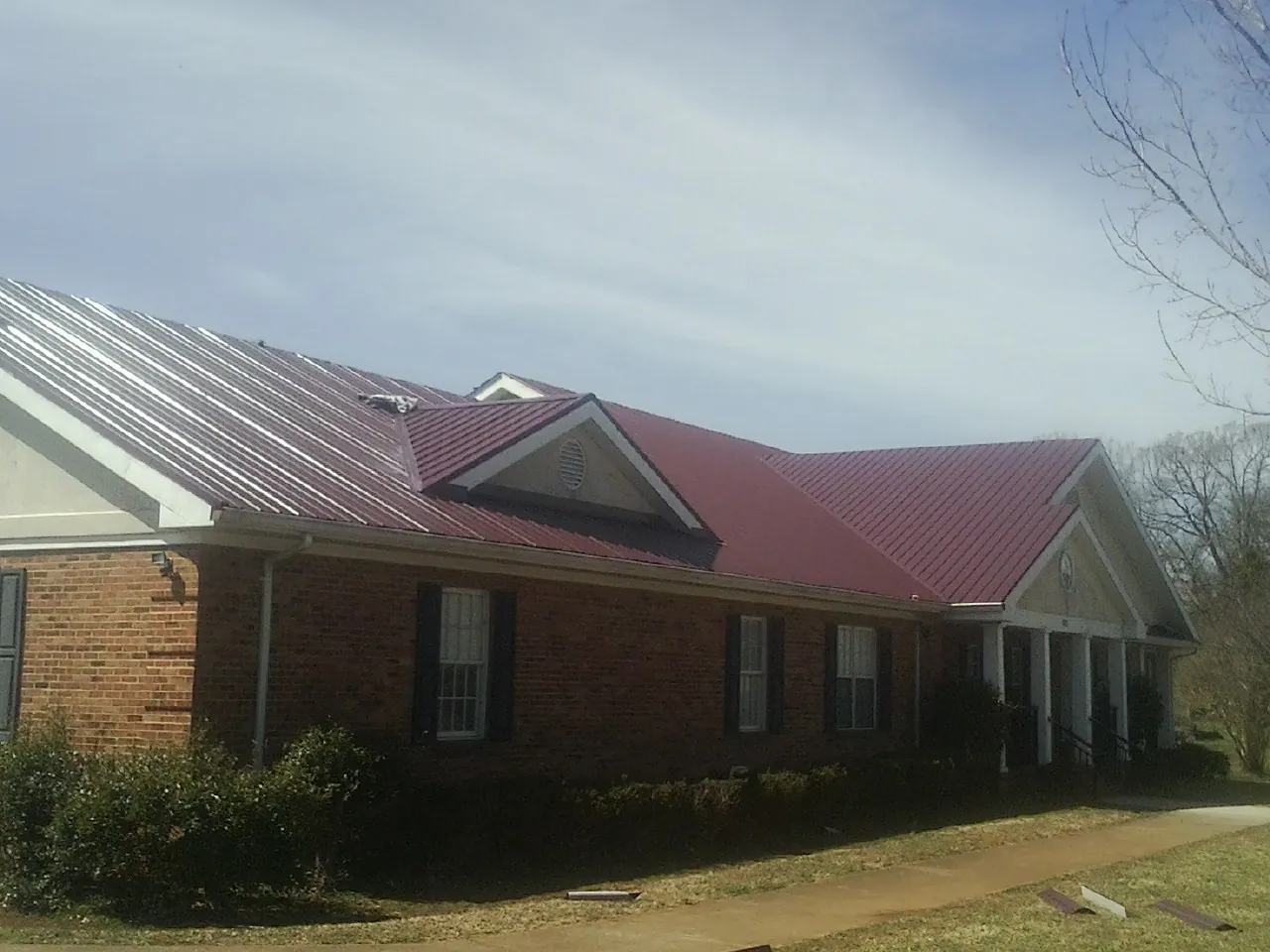 Red metal roof with gabled entries on a long brick building, from a Hail Damage Roof Repair job in Leggett