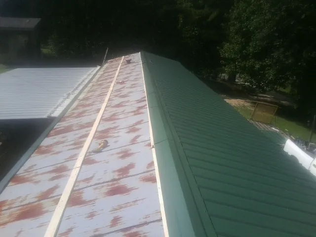Old rusted panels beside newly installed green metal roofing — Wind Damage Roof Repair by Roofing Brothers in Leggett