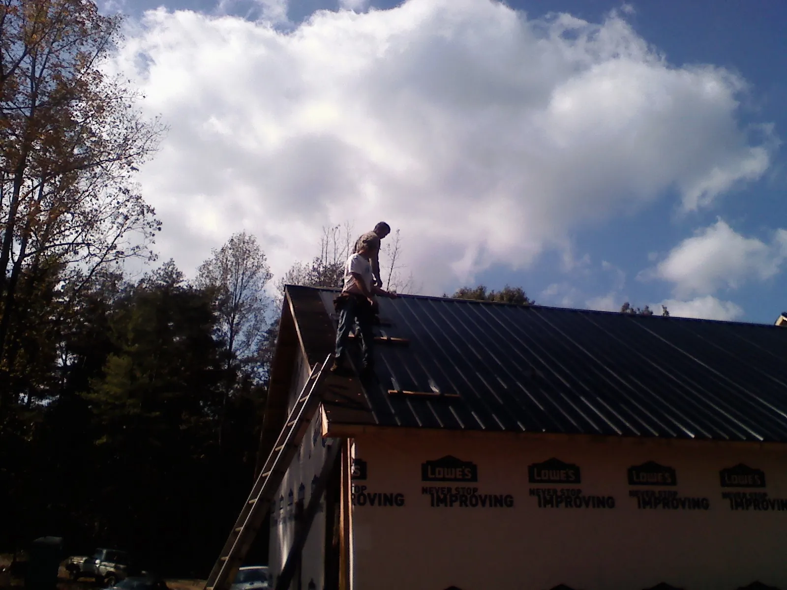 Roofer fastening dark metal panels high against a cloudy sky, from a Roof Inspection job in Leggett