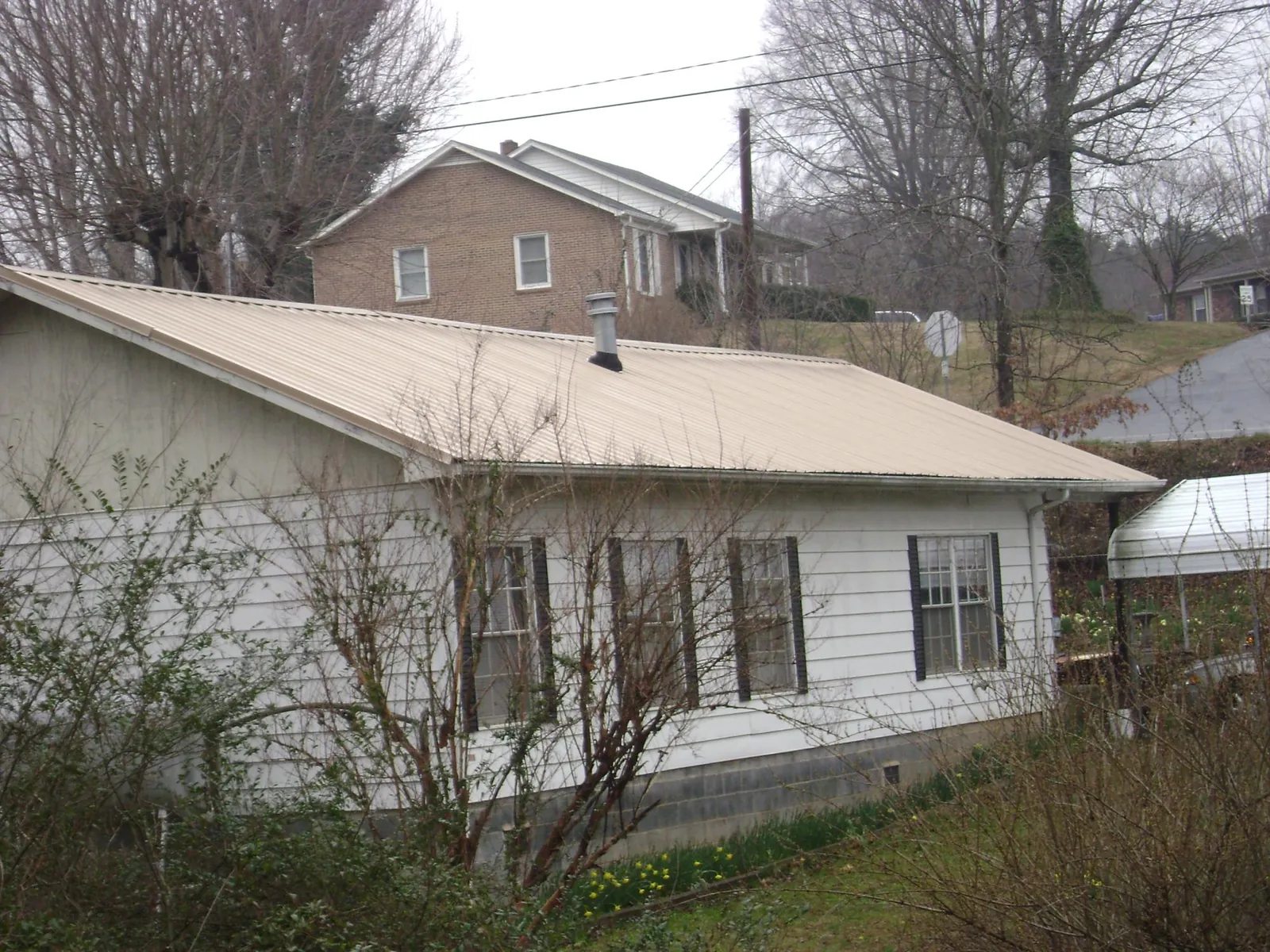 Tan metal roof on a white sided house set into a hillside — Commercial Roofing by Roofing Brothers in Leggett
